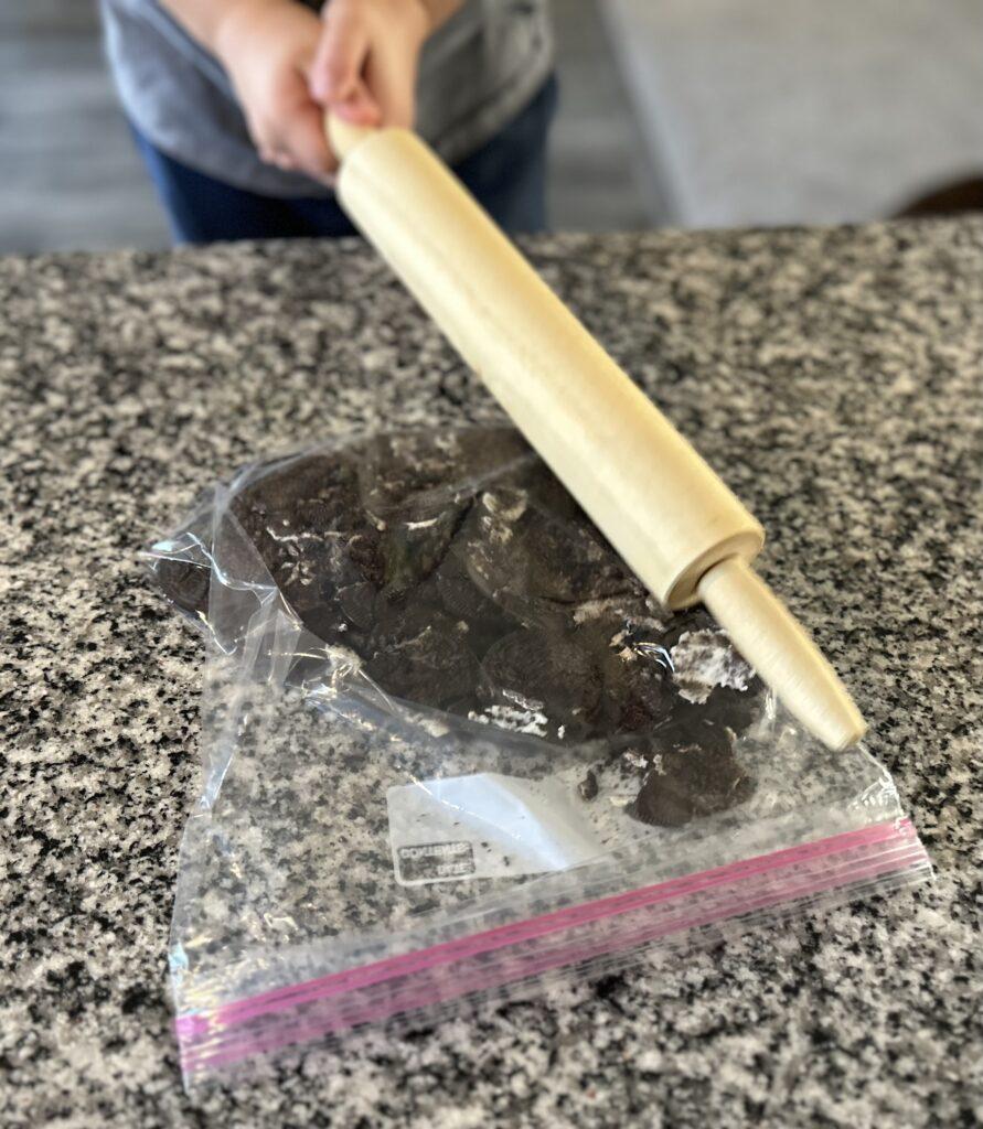 A child using a rolling pin to crush the Oreo cookies in a gallon size ziplock bag.