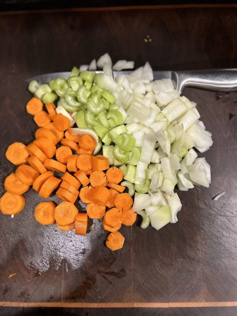 Chopped carrots, celery and onions on a cutting board for lentil hot dog soup. 