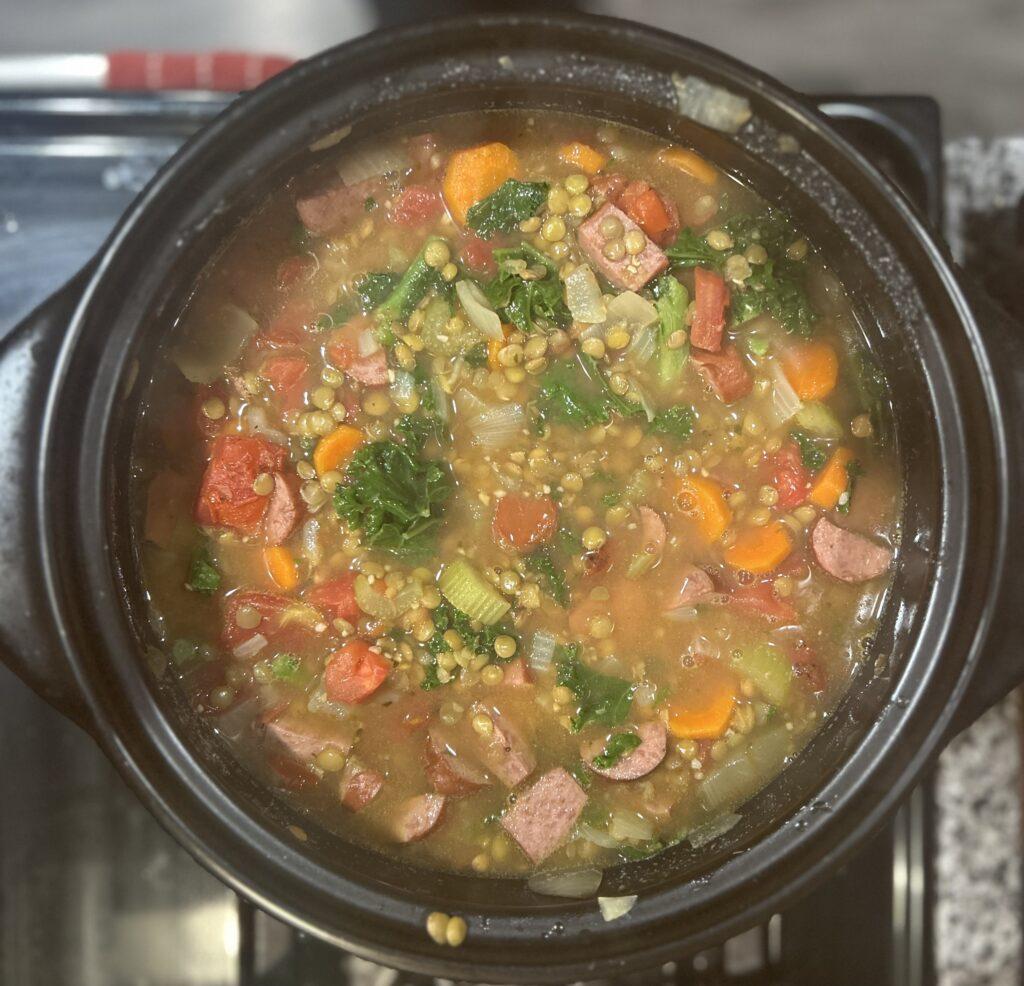 A pot of nearly finished hot dog soup with lentils simmering on the stove in a black dutch oven.