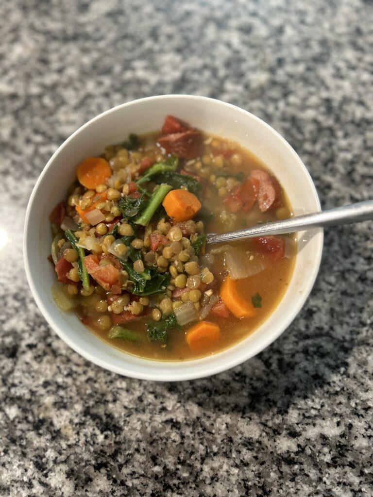 A white bowl with lentil hot dog soup and a spoon.