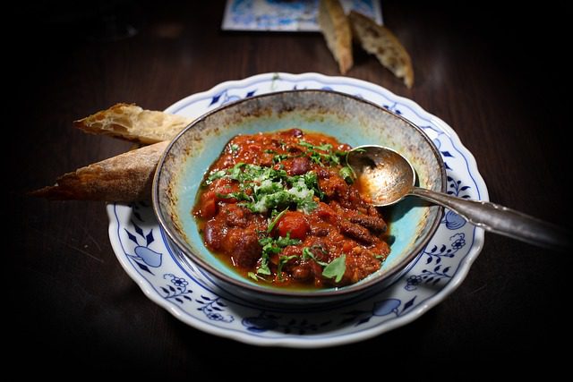 A bowl of over the top chili on a wooden table with bread for dipping.