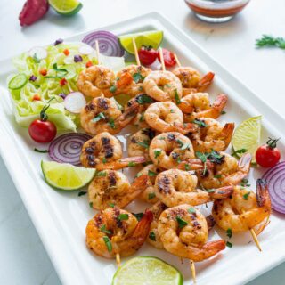 Chipotle Lime shrimp kabobs on a white plate with fresh slices of lime and red onion as a garnish.