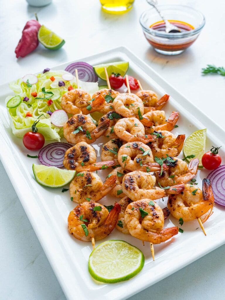 Chipotle Lim Shrimp kabobs on a white platter with fresh cherry tomatoes, lime slices and slices of red onion for a garnish.