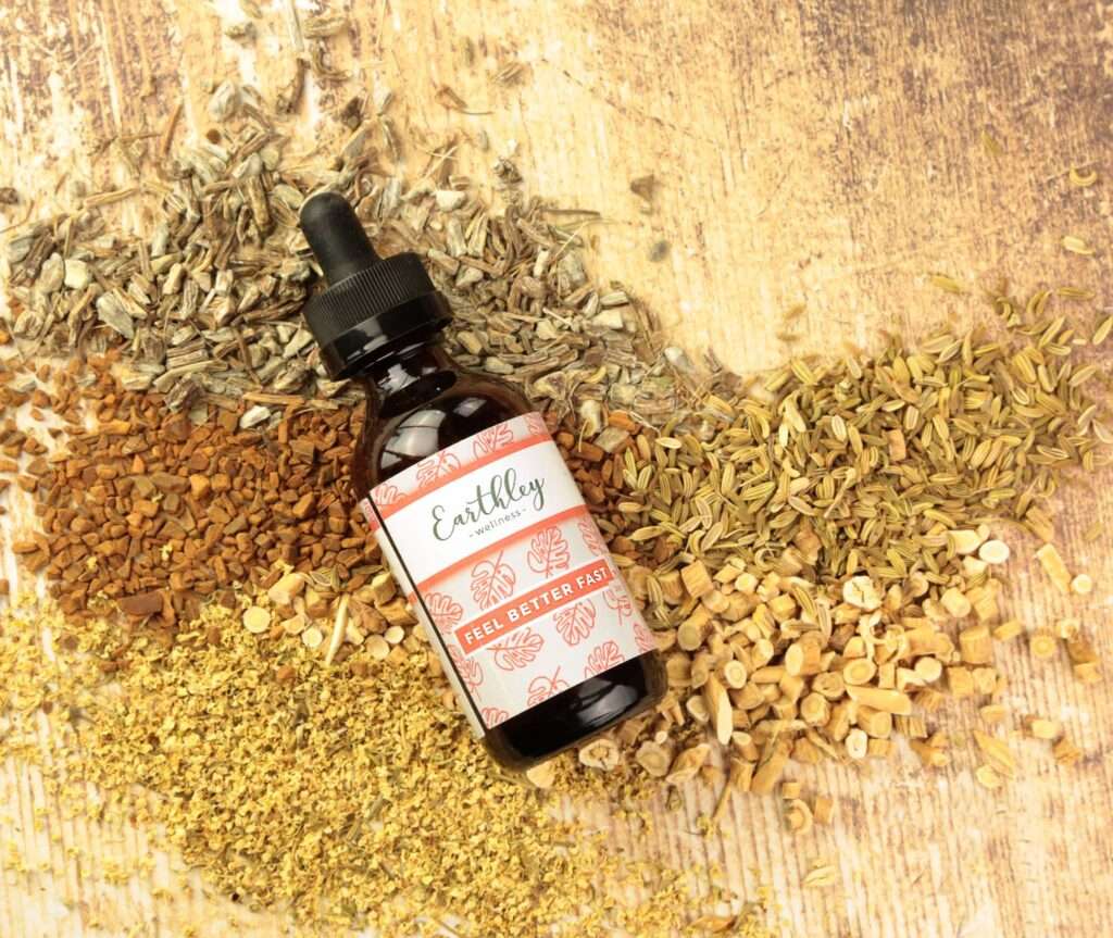 A bottle of Earthley Feel Better Fast surrounded by various herbs on a wooden counter top.