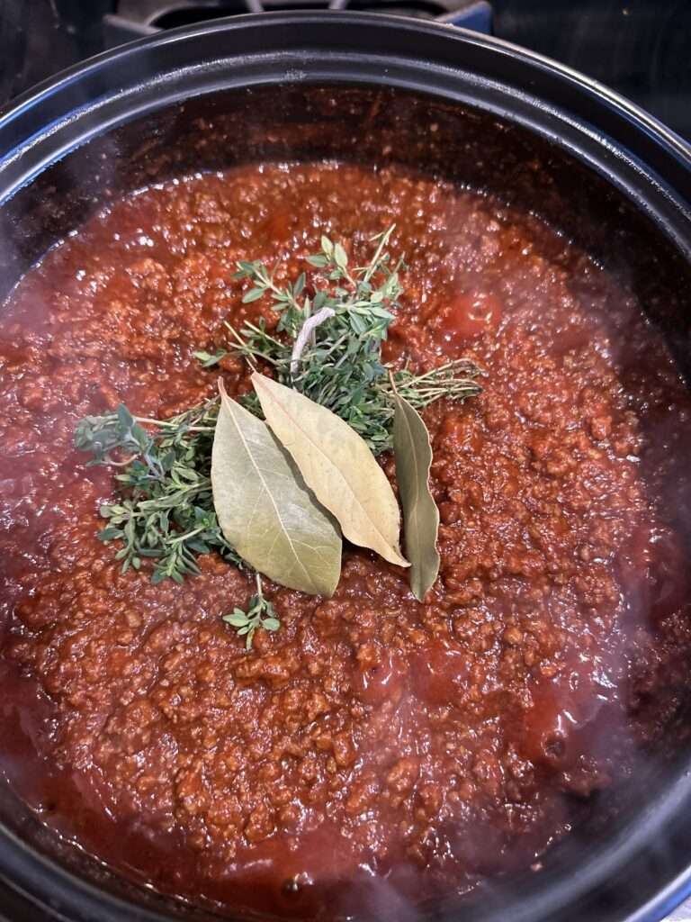 Homemade bolognese sauce in a dutch oven on the stove with fresh thyme and dried bay leaves on top.