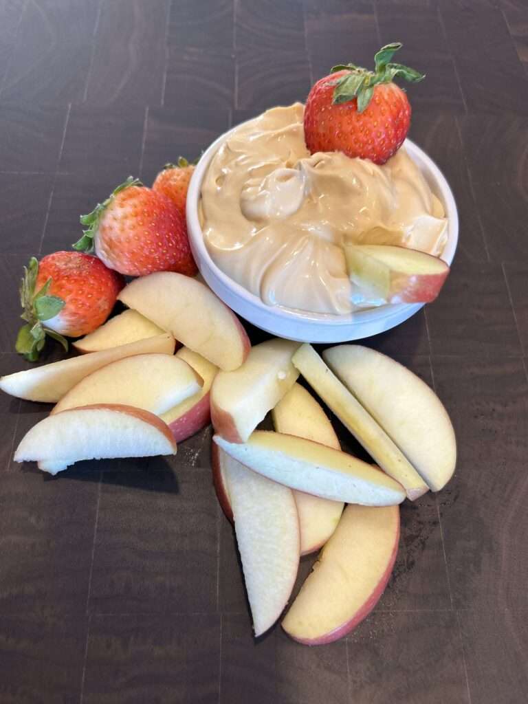 A bowl of 2 ingredient fruit dip with fresh strawberries and apple slices for dipping.