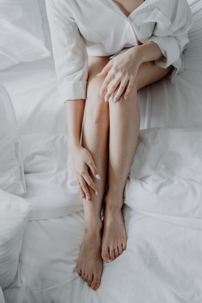 A women wearing a white shirt in a bed with white sheets with bare legs.