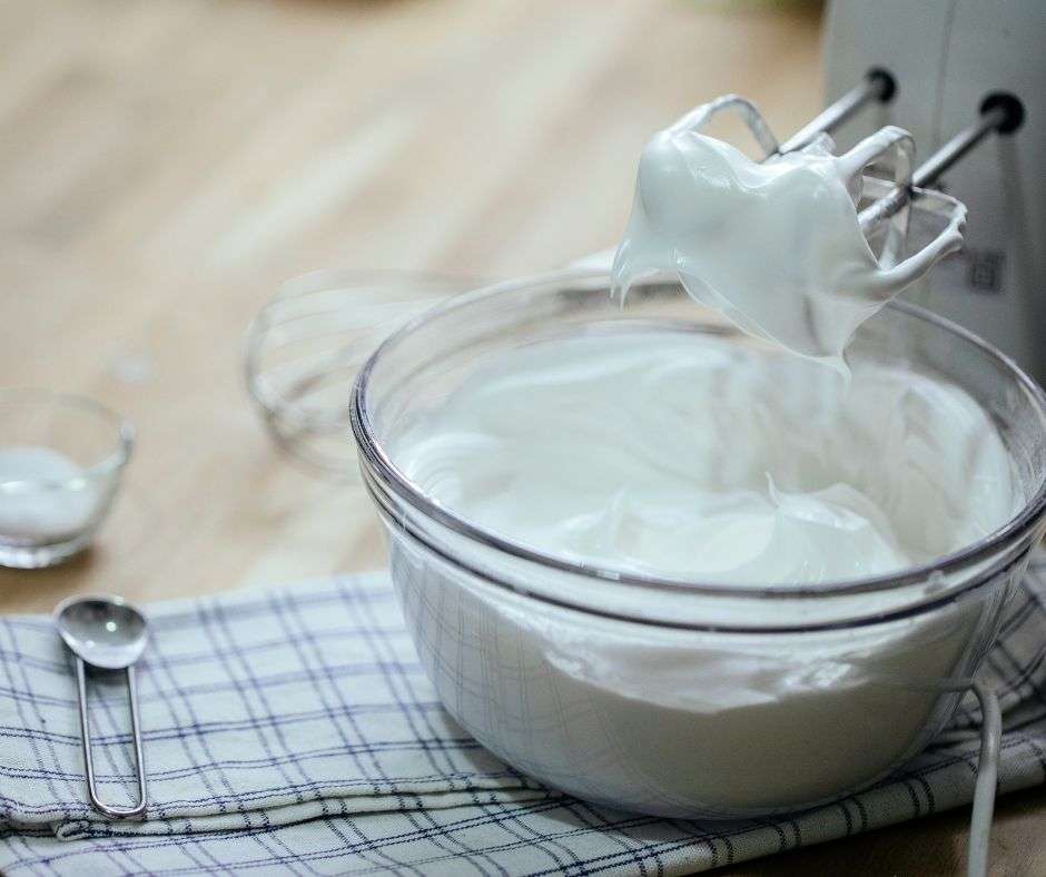 A large bowl of sugar free whipped cream being beaten with a hand mixer.