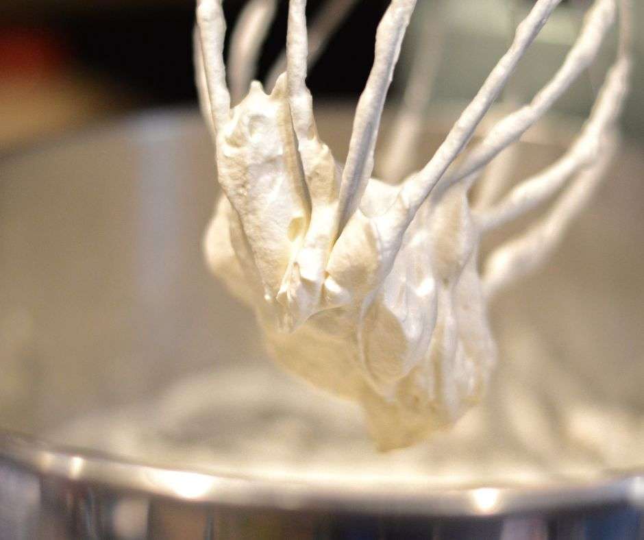 Soft Peaks of whipped cream on a standing mixer blade.