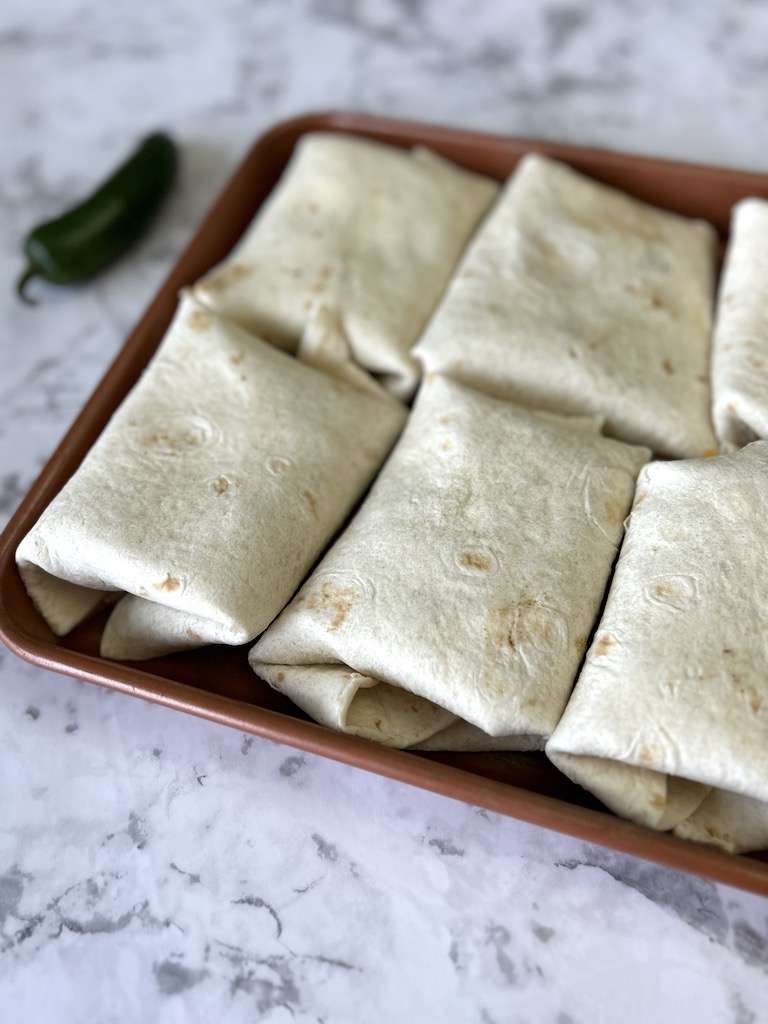 A cookie sheet filled with shredded beef chimichangas ready to be fried, air fried, or baked.