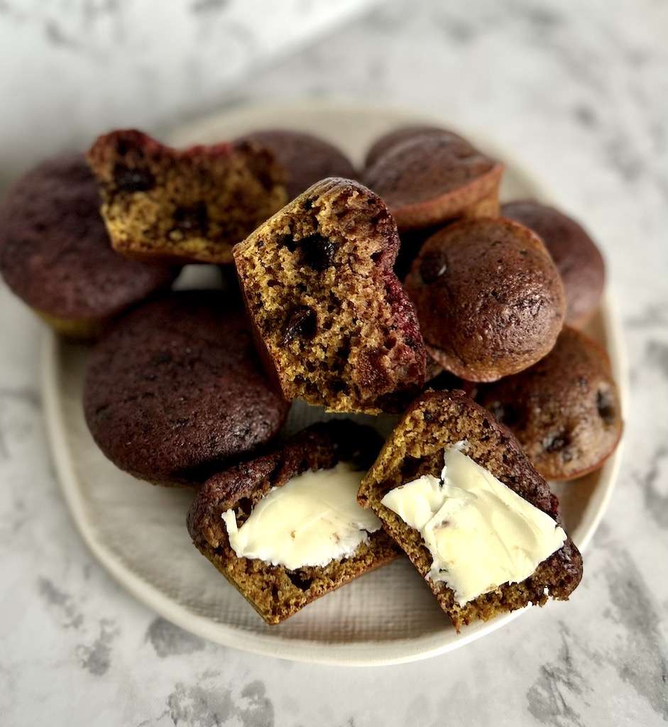 Chocolate beet muffins on a white plate with one muffin cut in half and buttererd.