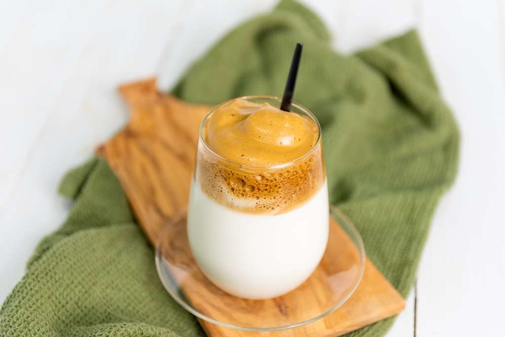 A glass of homemade dalgona latte with a spoon on a green napkin.