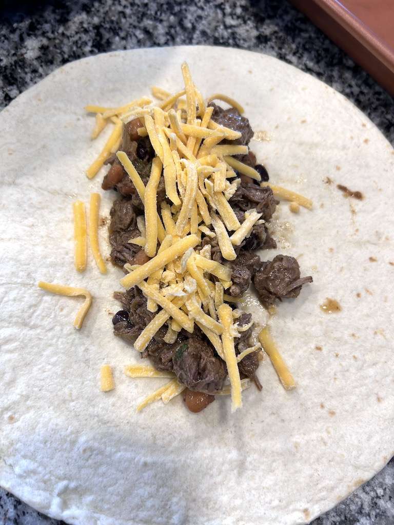 Add the shredded beef to the center of a large tortilla and top with shredded cheese.