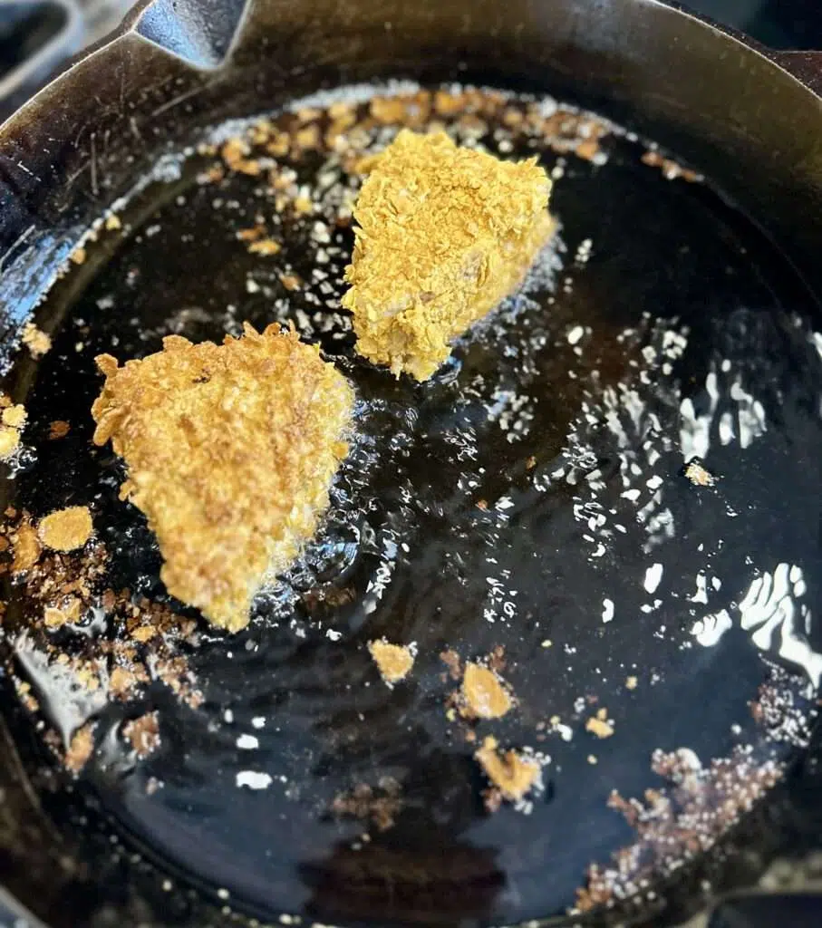 Two Nebraska cheese frenchee sandwiches frying in a cast iron skillet.