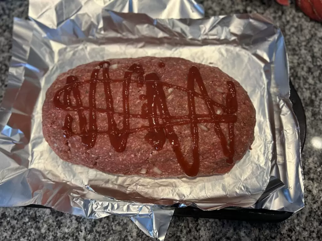 The Best Smoked Meatloaf Recipe A 6 pound meatloaf drizzled with ketchup on a tin foil lined cookie sheet ready to be smoked on the grill.