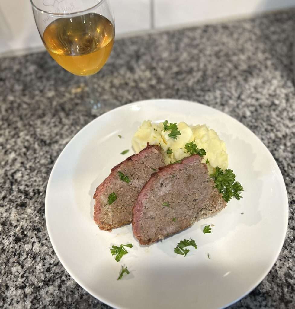 Two slices of smoked meatloaf with a side of mashed potatoes on a white plate garnished with fresh parsley.