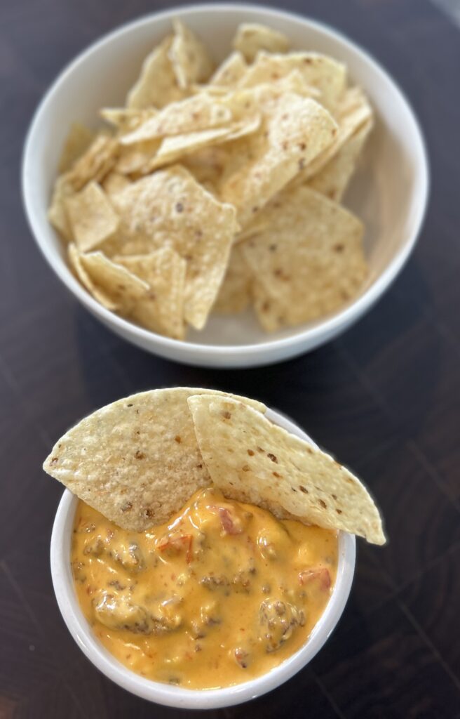 A white bowl of tortilla chips next to another bowl of slow cooker chorizo queso dip.