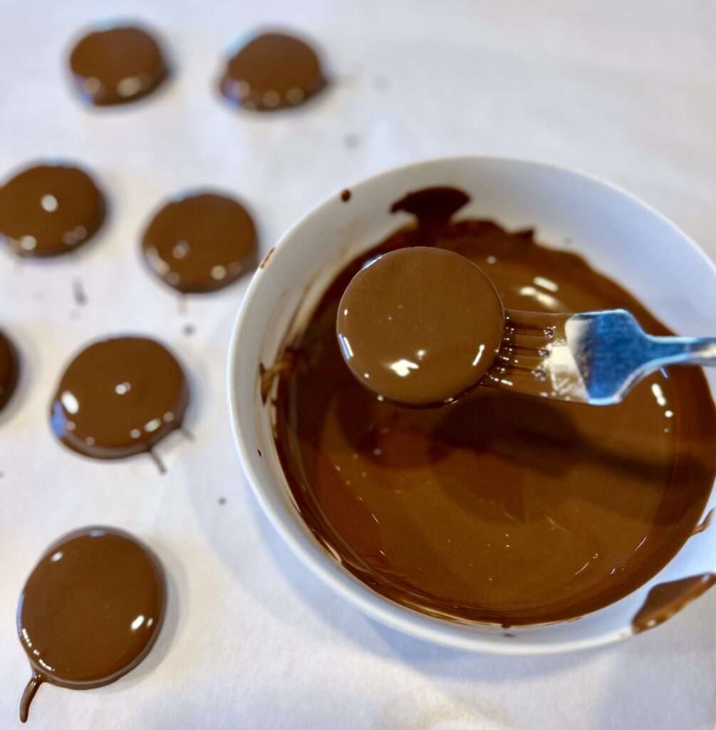 Using a fork to dip the Thin Oreo cookie into the melted creme de menthe chips to make homemade thin mints.