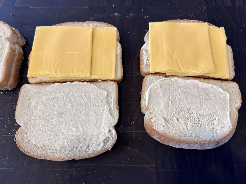 Two cheese frenchees being assembled with mayo and cheese slices.
