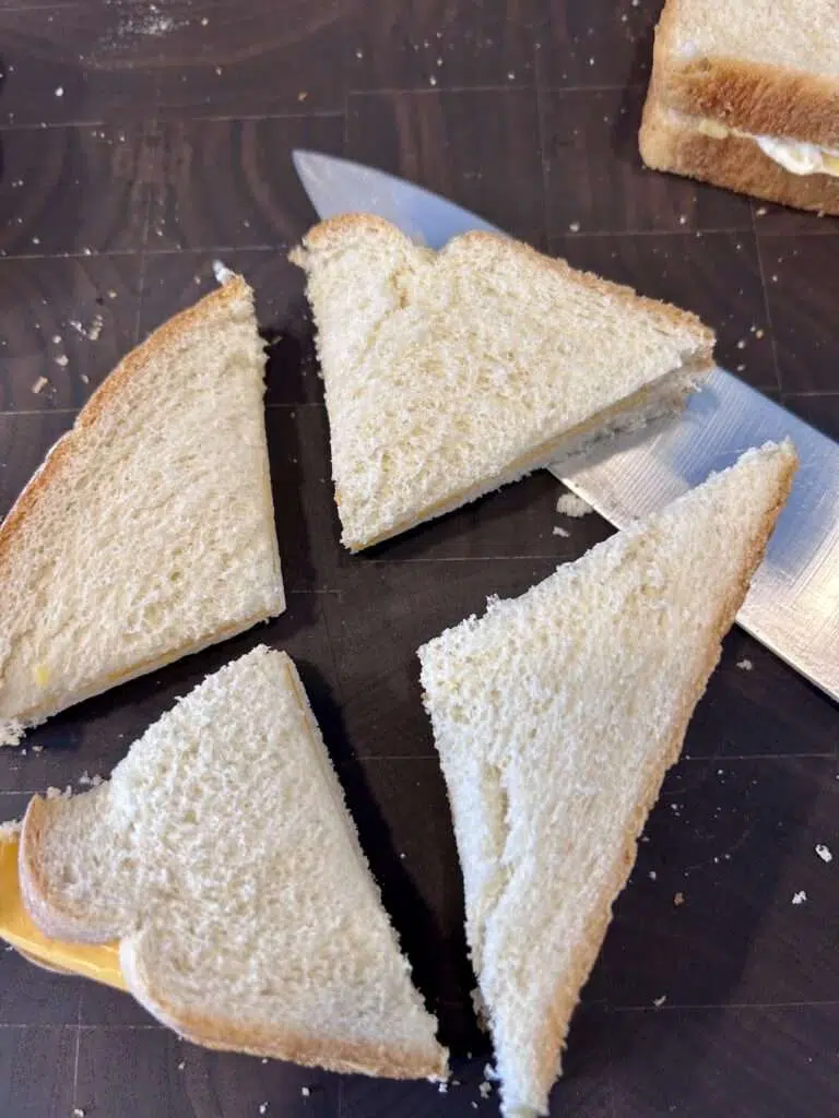 Cutting the assembled cheese frenchee sandwiches into quarters.