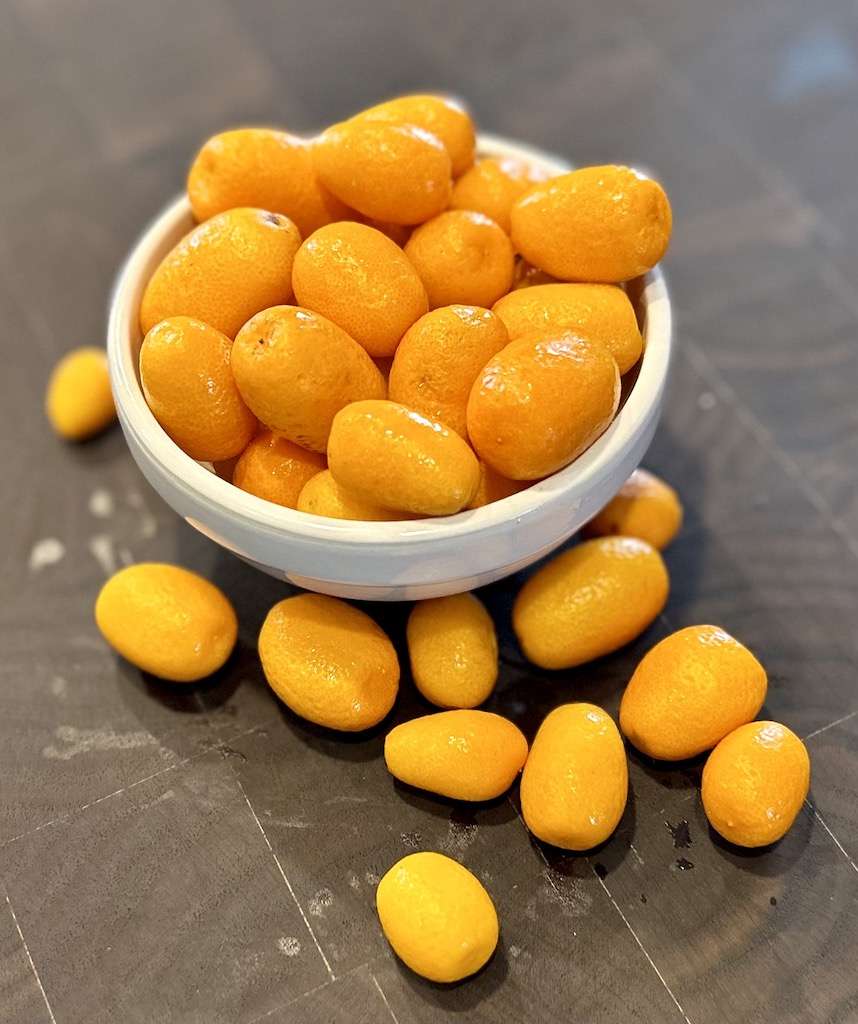 Kumquats in a bowl spilling over onto a dark wooden cutting board.