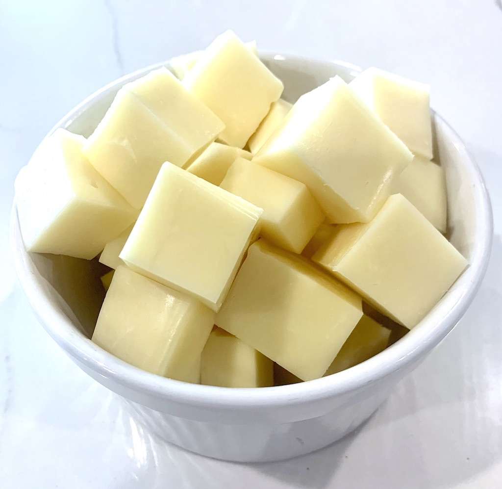A white bowl of cubed mozzarella cheese.