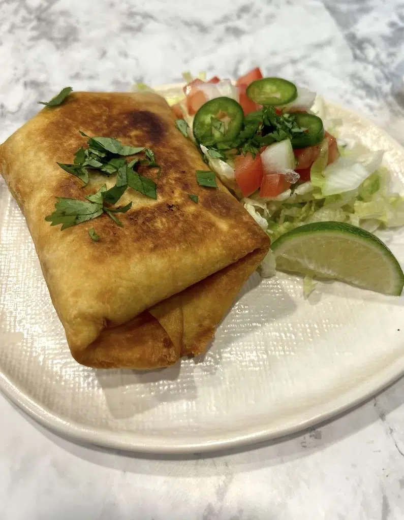 A fried shredded beef chimichanga on a plate with lettuce, tomatoes, jalapeños, and fresh lime slices for toppings.