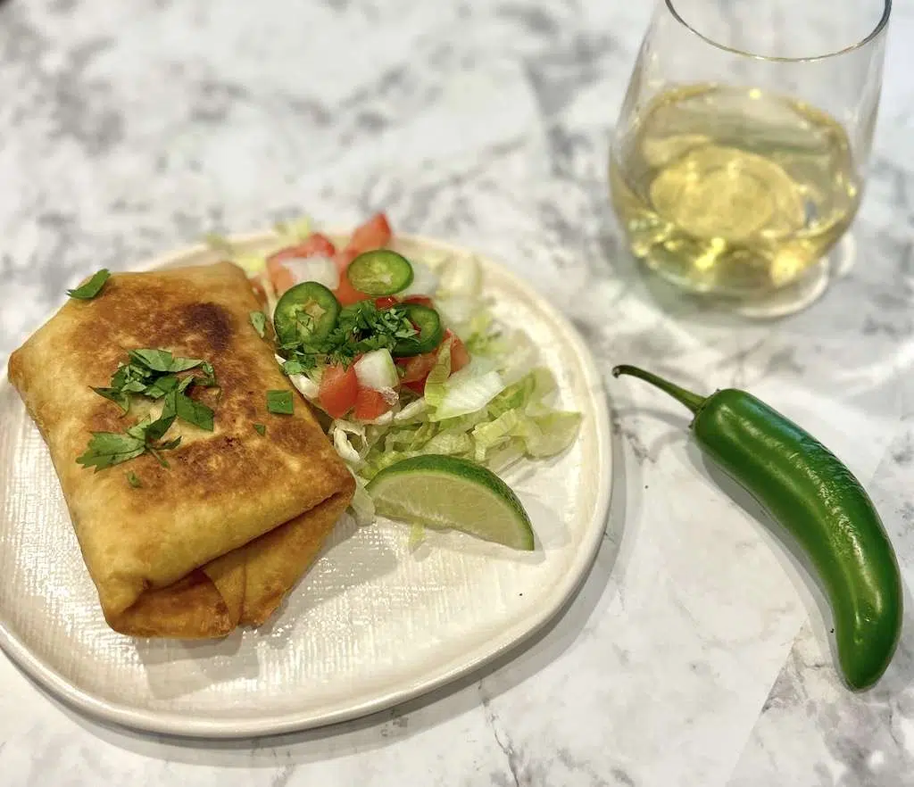 A deep fried shredded beef chimichanga on a plate with toppings including lettuce, tomatoes, and fresh lime slices.