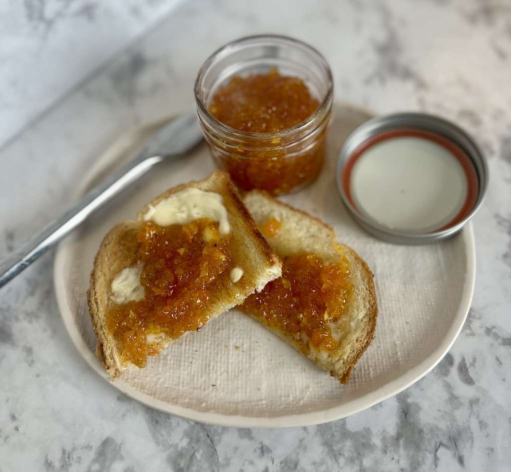 Kumquat Marmalade in a mason jar on a plate with buttered toast topped with kumquat jam.