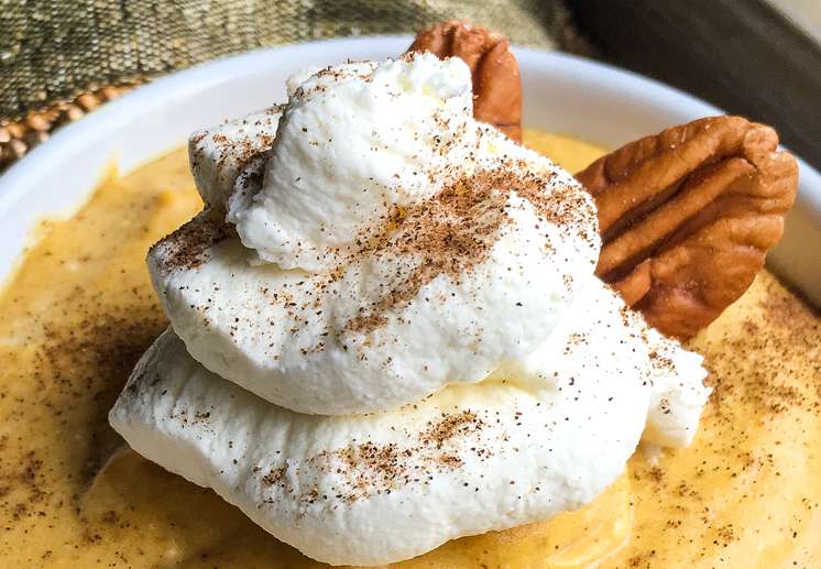 A serving of sugar free pumpkin mousse topped with maple whipped cream and garnished with nutmeg and pecans.