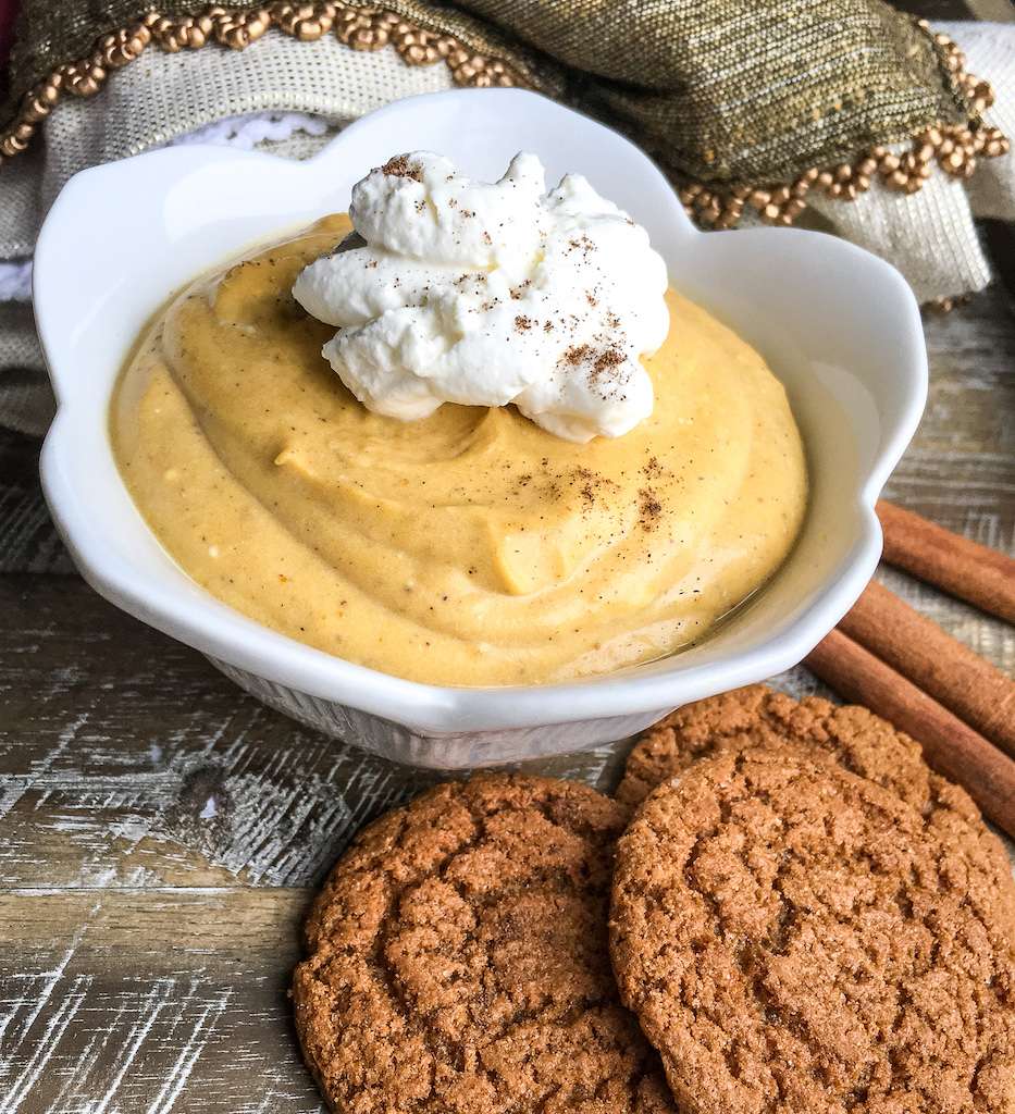 A white bowl with sugar free pumpkin mousse garnished with fresh whipped cream.