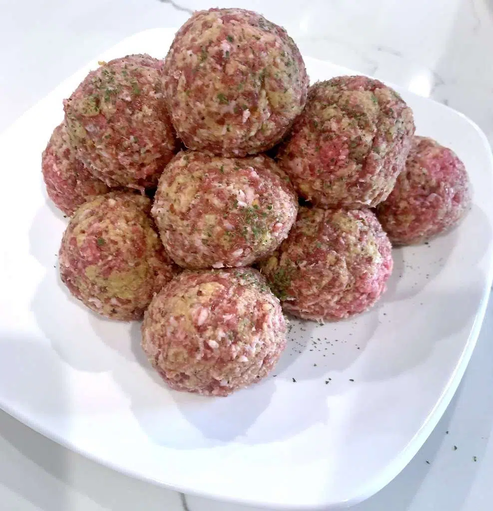 Uncooked mozzarella stuffed meatballs on a plate before placing them in the slow cooker.