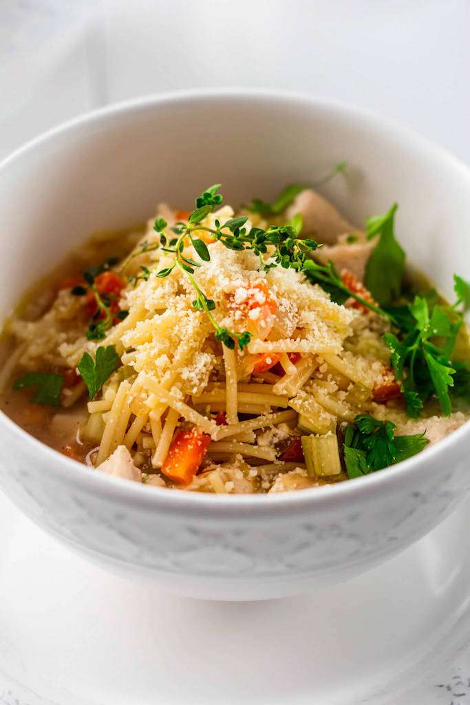 A close up photo of chicken fideo soup in a white bowl garnished with fresh thyme.