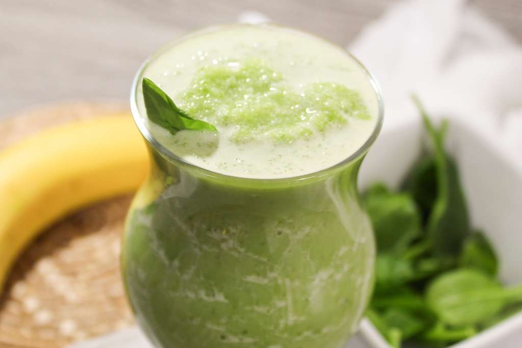 A close up view of a frosting spinach and banana smoothie with a spinach leaf for a garnish.
