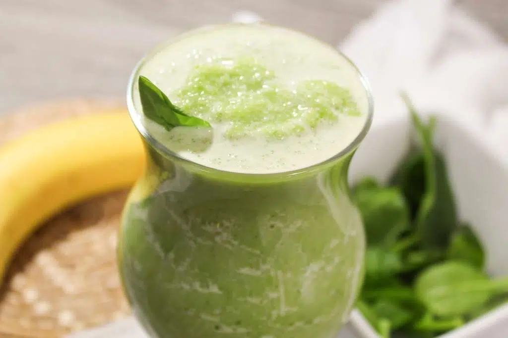 Refreshing Spinach Banana Smoothie A close up view of a frosting spinach and banana smoothie with a spinach leaf for a garnish.