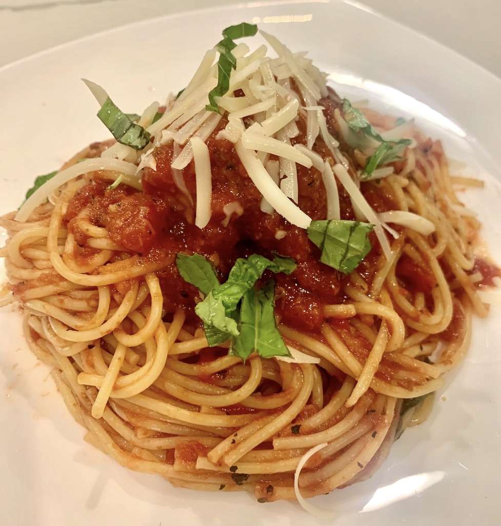 A plate of spaghetti with a quick marinara sauce garnished with fresh parmesan cheese and basil.