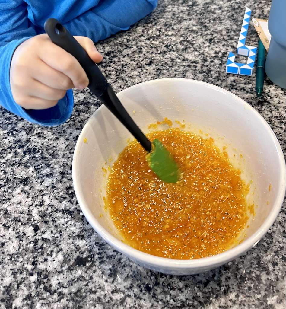 One of my sons stirring the easy kumquat marmalade in a bowl with a spatula.