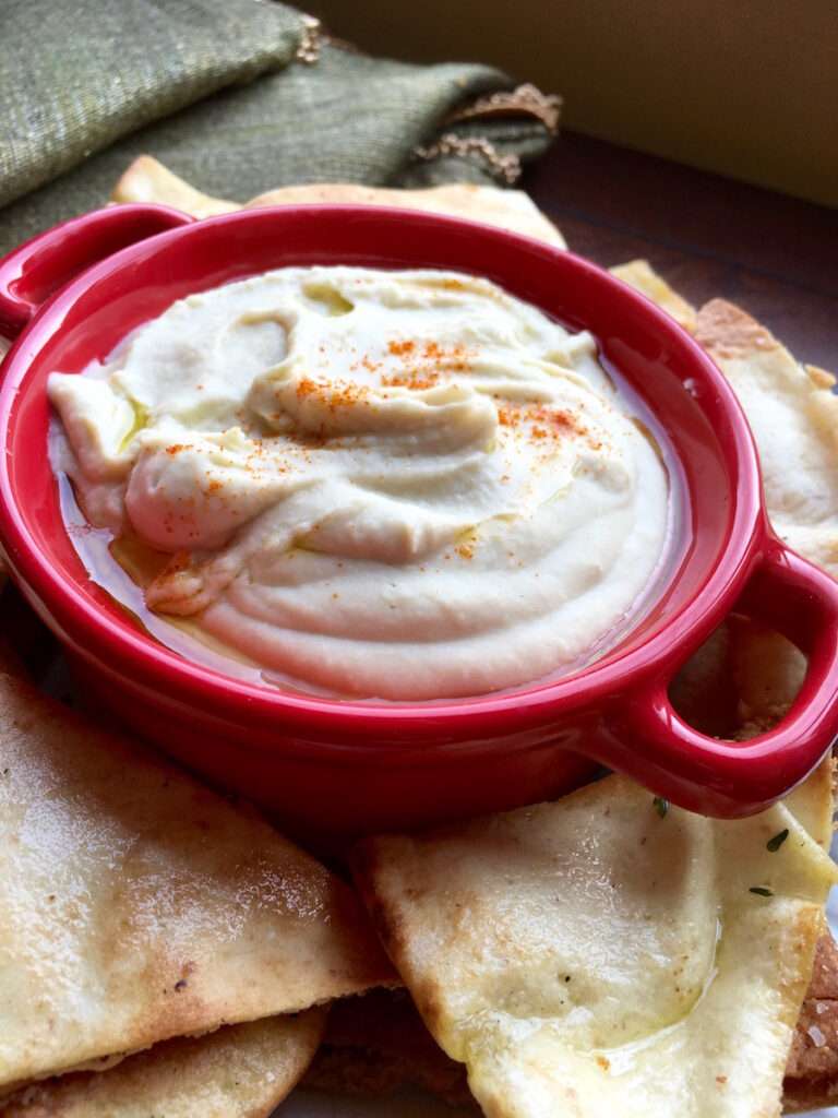 White Bean Dip  in a red bowl surrounded by seasoned pita chips.