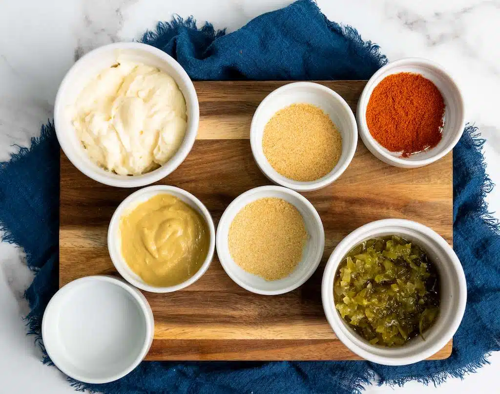 A wooden cutting board with bowls of big mac sauce ingredients including relish, mustard, mayonnaise and various seasonings.