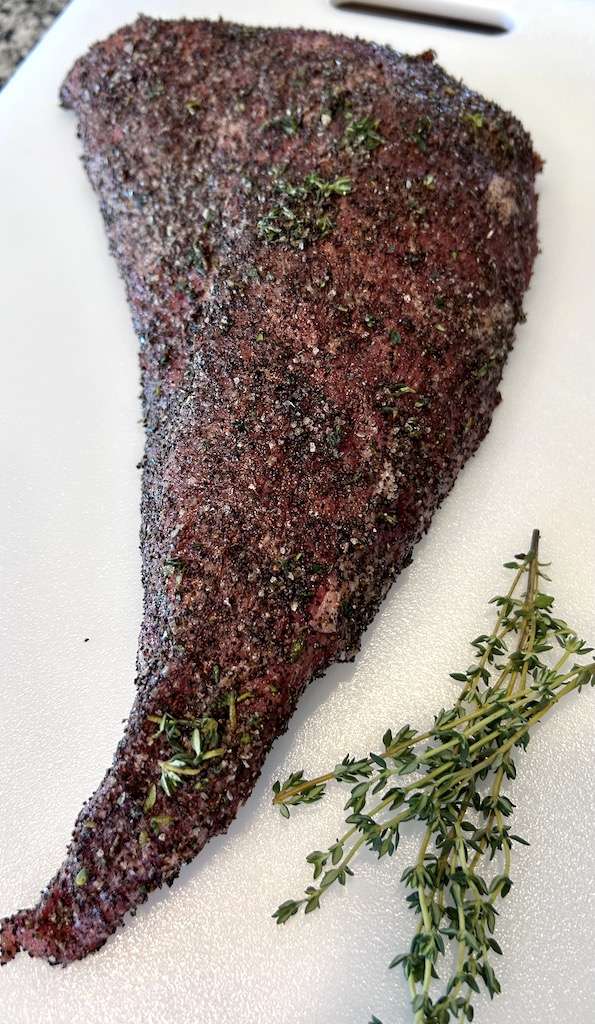 Coffee Rubbed Tri-Tip with the coffee rub on a white cutting board with fresh thyme sprigs.