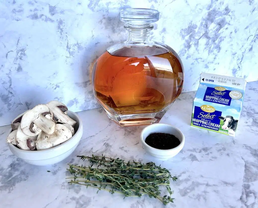 Coffee-Rubbed Tri-Tip with Bourbon Mushroom Cream Sauce Coffee Rubbed Tri-Tip Steak Ingredients on a marble counter top including a bourbon decanter, heavy whipping cream. fresh sliced mushrooms, ground coffee, and fresh thyme.