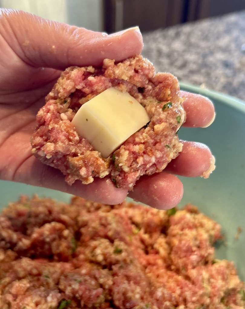 A portion of the seasoned meat mixture with a cube of mozzarella cheese in the center forming a stuffed meatball.