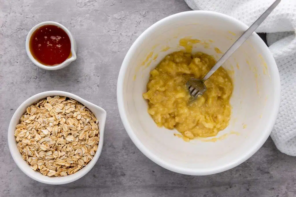 Granola Berry Cups - A Delicious Treat Oats and honey next to a mashed banana in a white mixing bowl.
