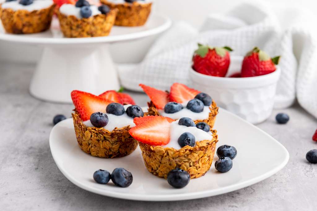 Granola Berry Cups on a white plate with a bowl of fresh strawberries behind.