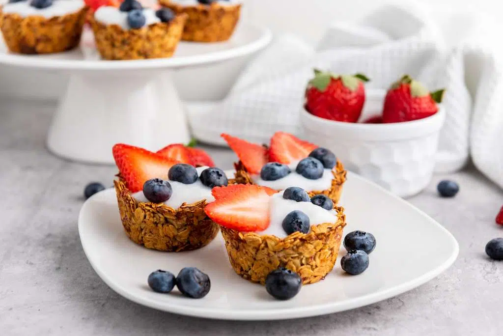 Granola Berry Cups - A Delicious Treat Granola Berry Cups on a white plate with a bowl of fresh strawberries behind.