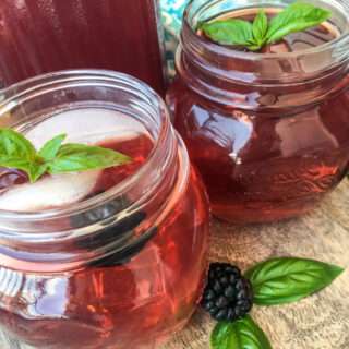 Two glasses of blackberry iced tea garnished with basil and fresh blackberries.
