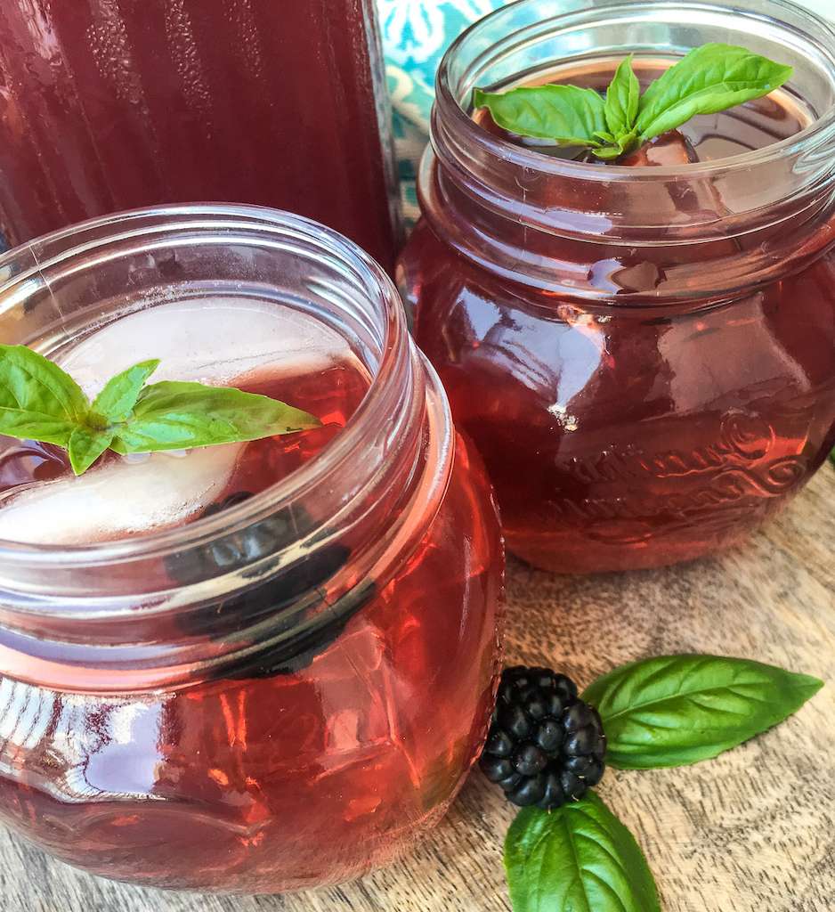 Two glasses of blackberry iced tea garnished with basil and fresh blackberries.