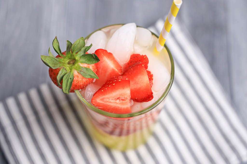 Looking down into a tall glass of Limoncello strawberry lemonade with fresh strawberries, ice and a paper straw.