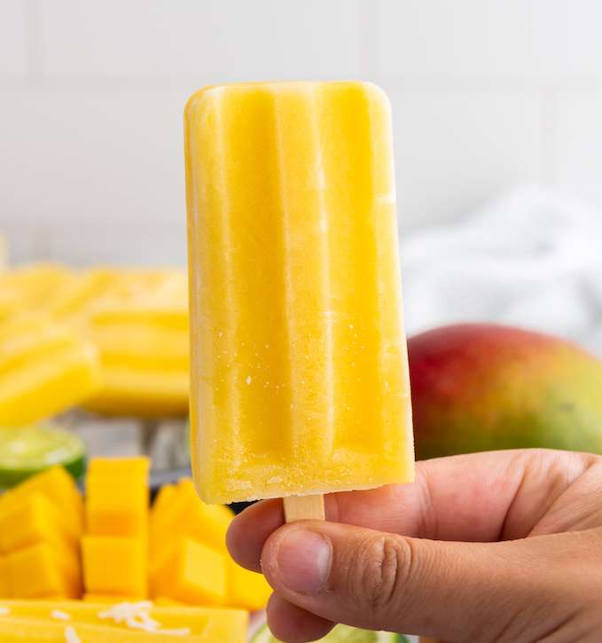 Mango Lime Popsicle on a stick with diced mangos in the background.