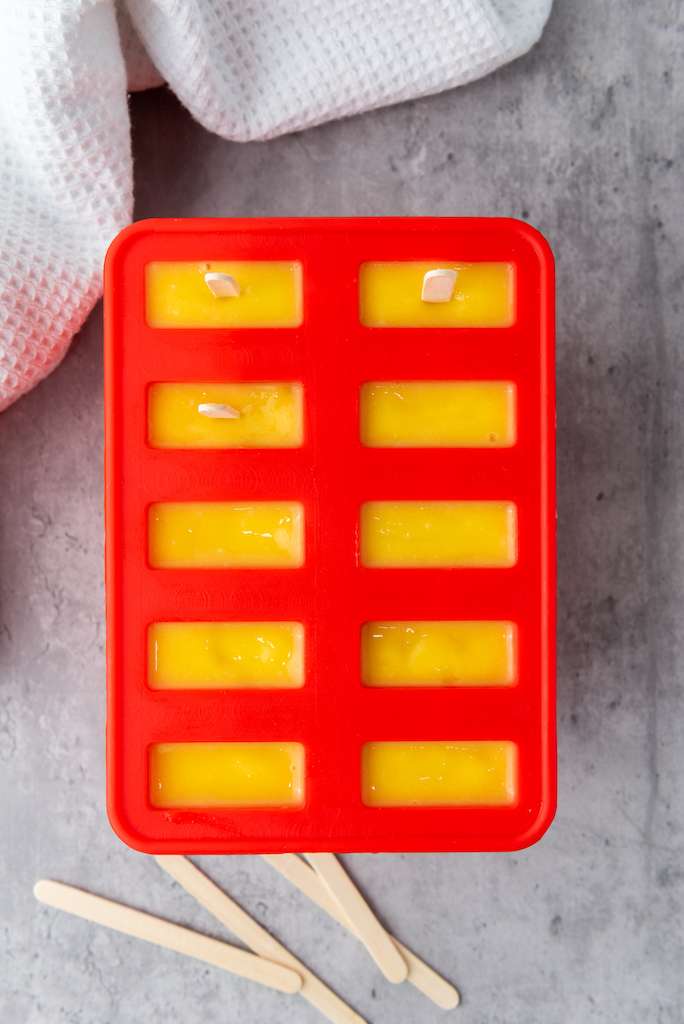 Mango lime popsicles in a popsicle mold with a few stick inserted.